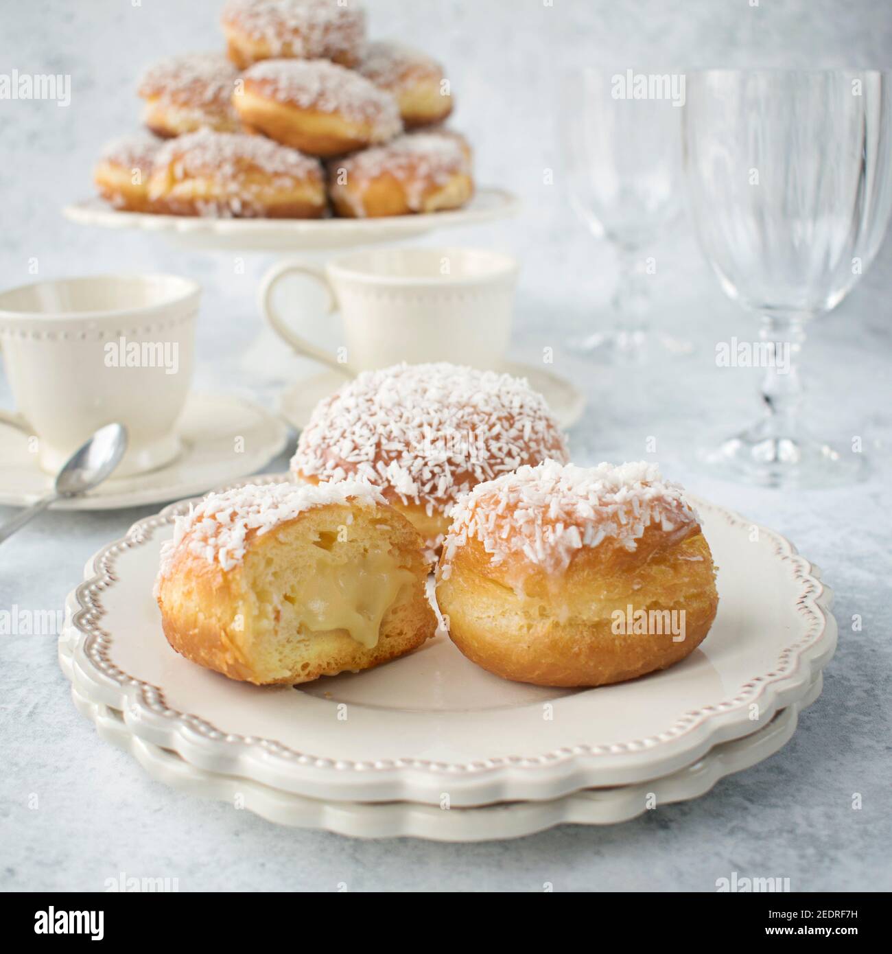 Donuts with frosting and coconut and white chocolate pudding filling. Appetizing sweet cakes on a white plate. Stock Photo