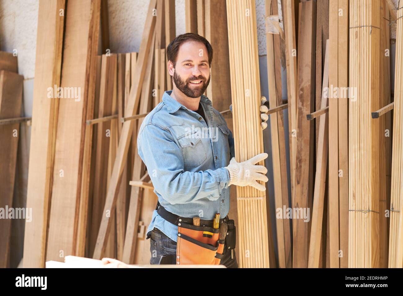 Young craftsman as a carpenter apprentice carries boards in the wood store of the joinery Stock Photo