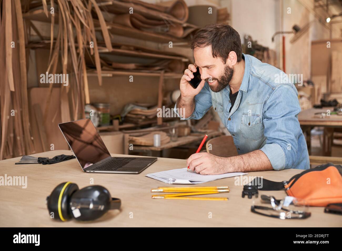 Young handyman man using laptop computer while talking to customer on the phone Stock Photo