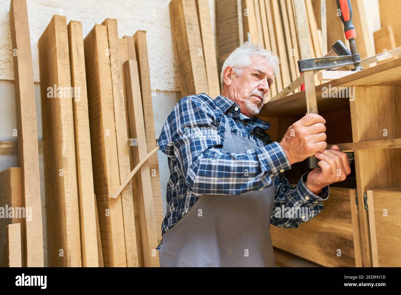 Older craftsman as a cabinet maker attaches screw clamp to a cabinet Stock Photo