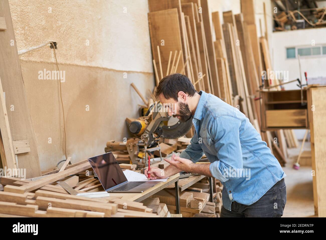 Young handyman during video chat on laptop computer in carpentry Stock Photo