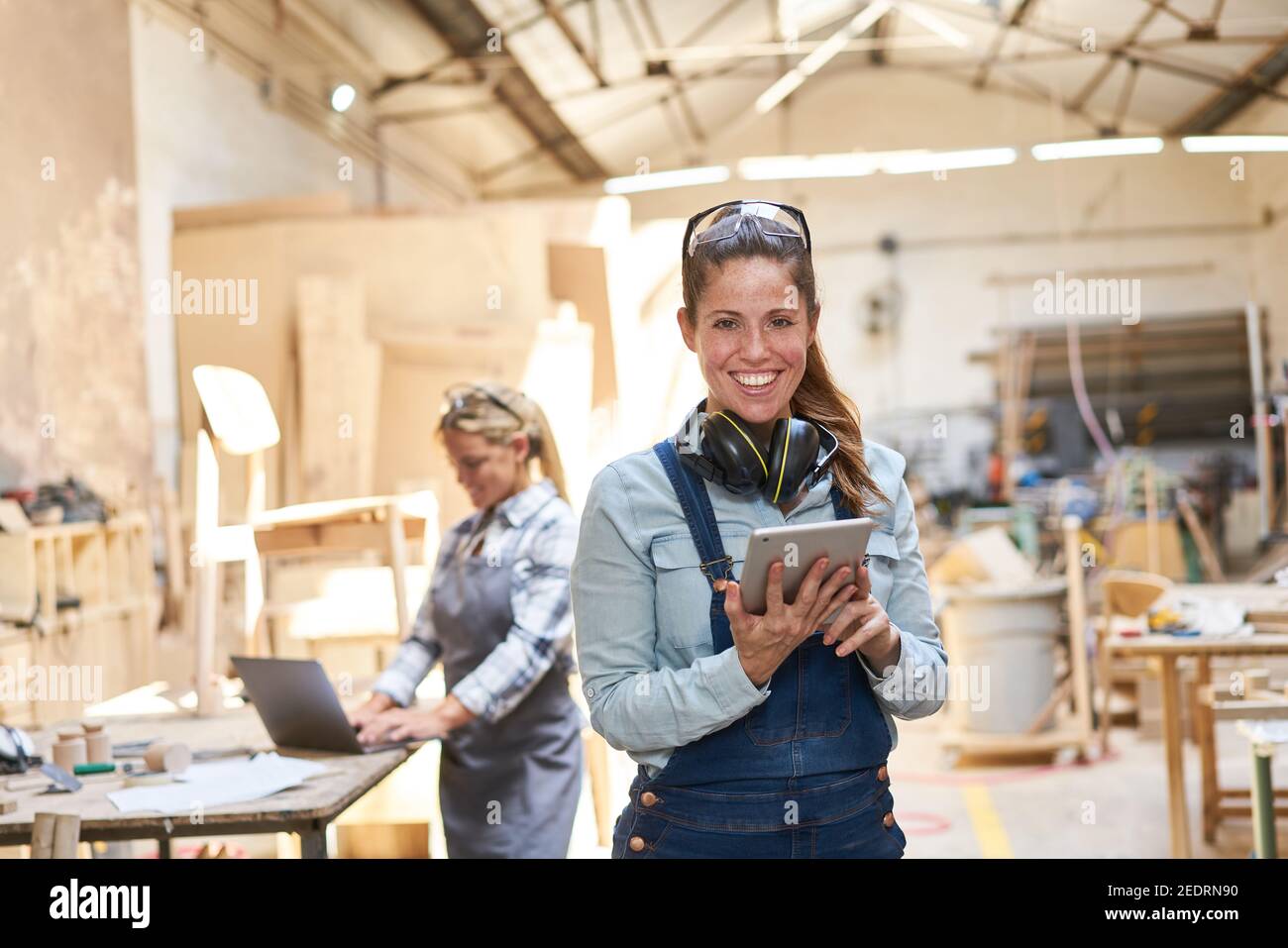Smiling craftsman woman in carpentry workshop using tablet computer Stock Photo