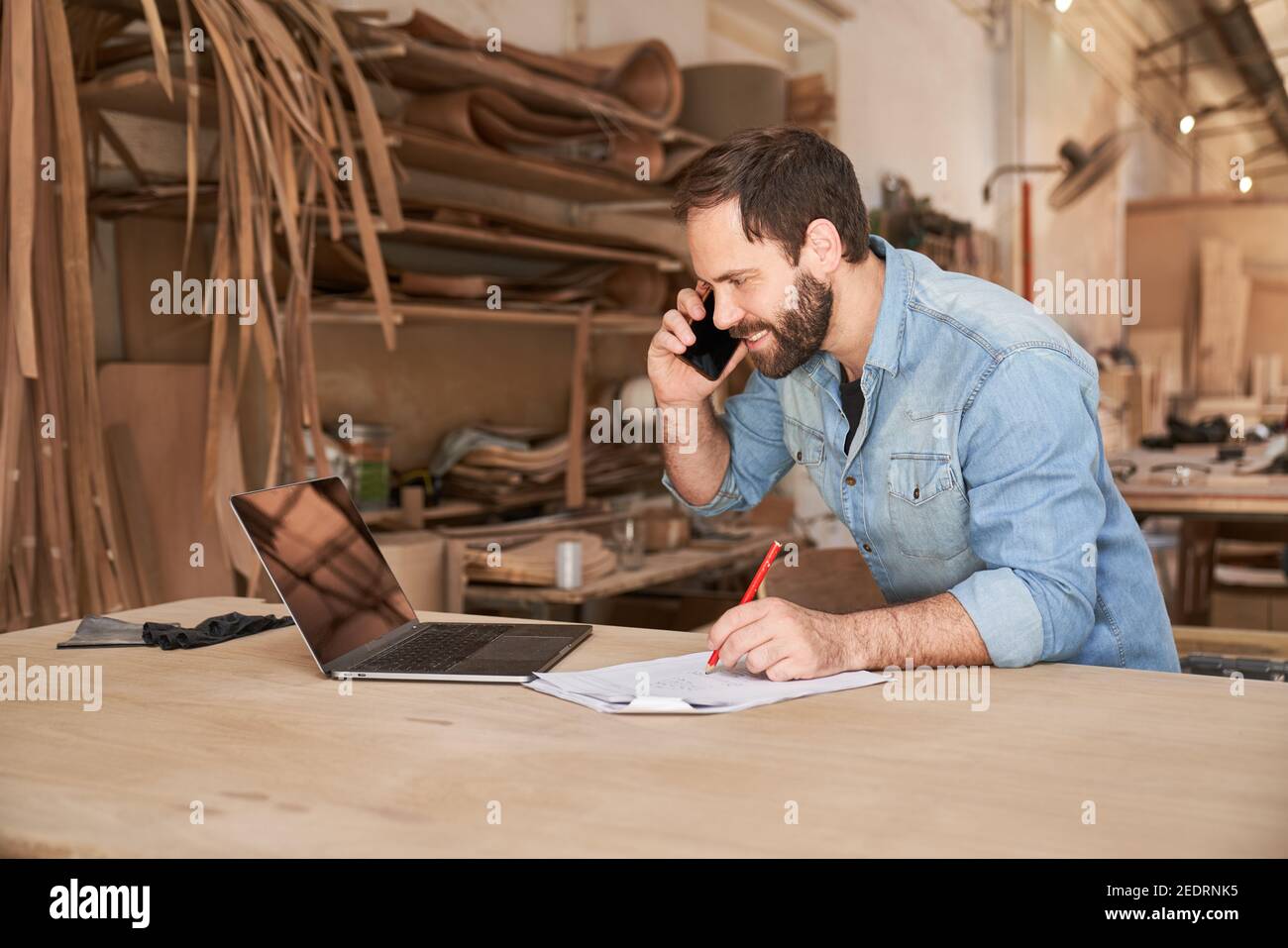 Handyman using phone and laptop computer when scheduling in workshop Stock Photo