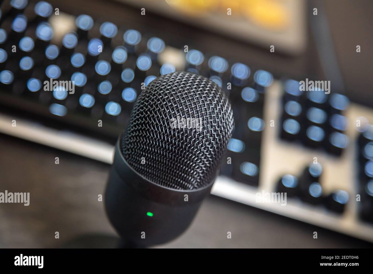 Tilted mic condenser black metallic, blur keyboard and monitor background. Digital technology concept. Communication with pc through mike, recording, Stock Photo