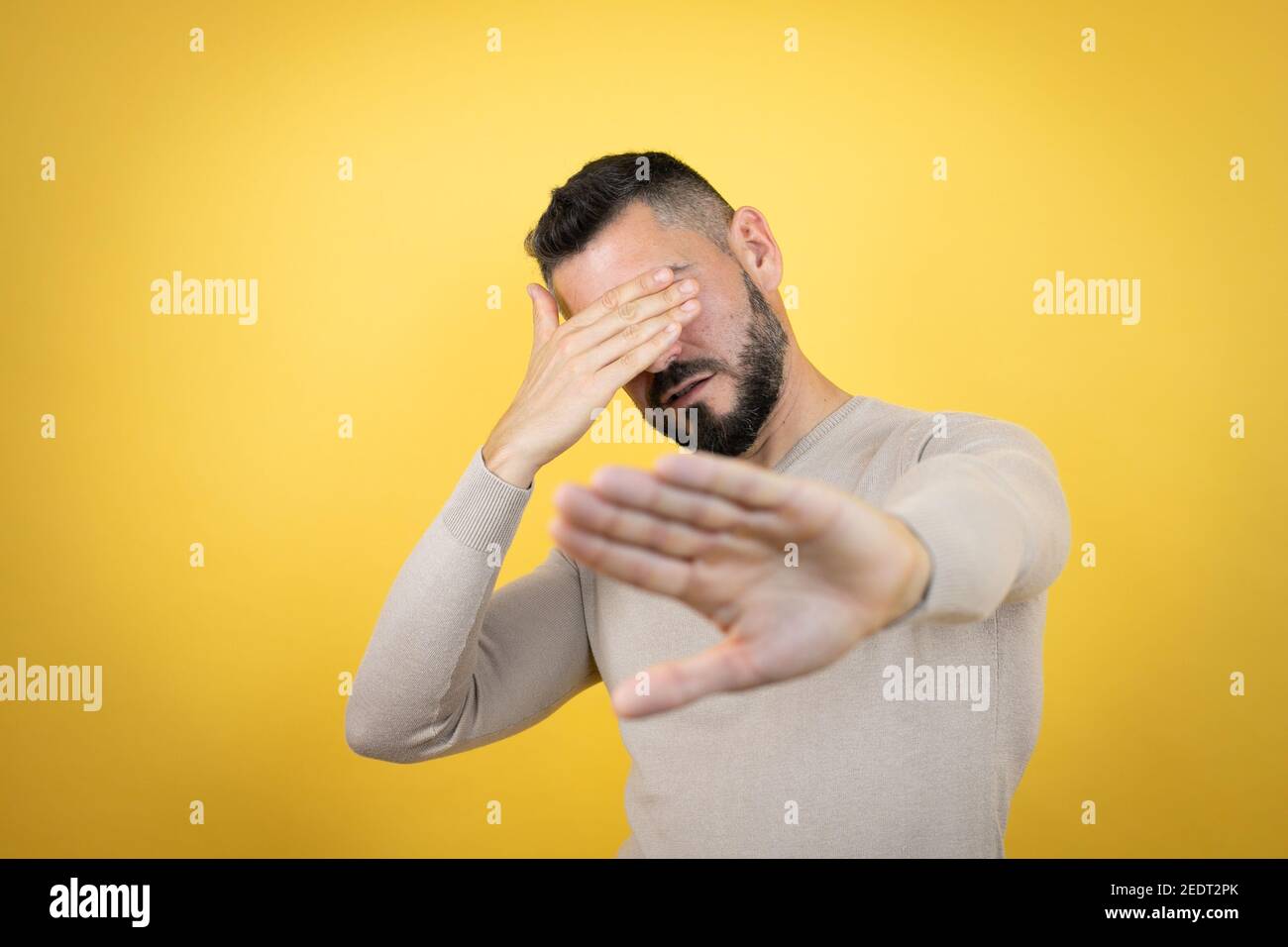 Handsome man with beard wearing sweater over yellow background covering eyes with hands and doing stop gesture with sad and fear expression. Embarrass Stock Photo