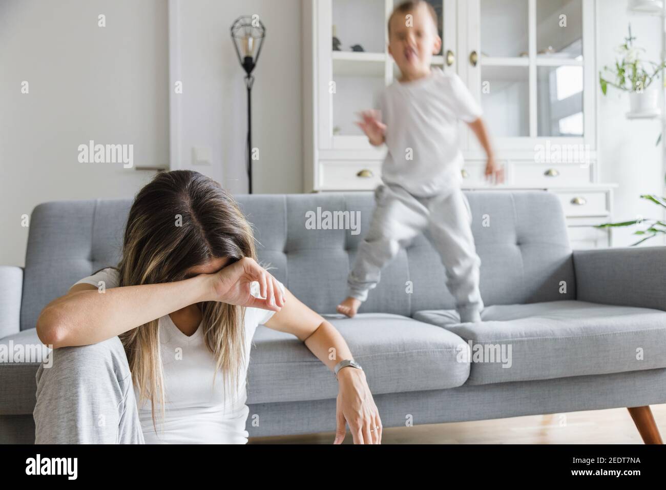 Hyperactive child and his tired and sad mother at home Stock Photo