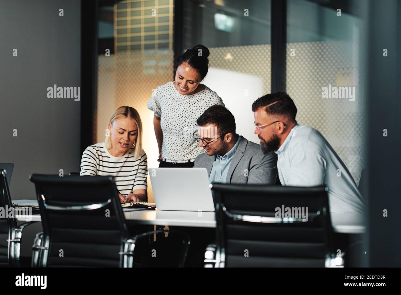 Group of smiling businesspeople working together on a laptop and discussing paperwork at a table during a meeting in an office boardroom Stock Photo