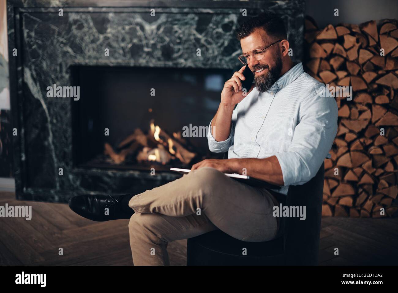 Smiling young businessman sitting in the lounge area of an office and talking with a client over the phone Stock Photo