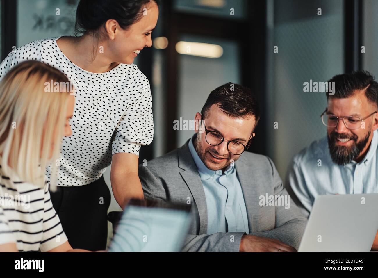 Smiling group of businesspeople working together on a laptop and discussing paperwork at a boardroom table in an office Stock Photo