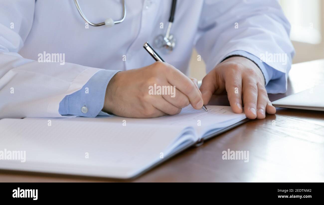 Close up male doctor writing notes in registry book. Stock Photo