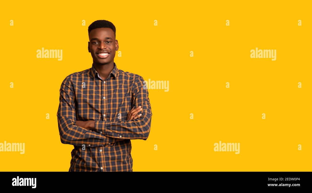 Positive Young Black Guy Posing With Folded Arms Over Yellow Studio Backgound Stock Photo