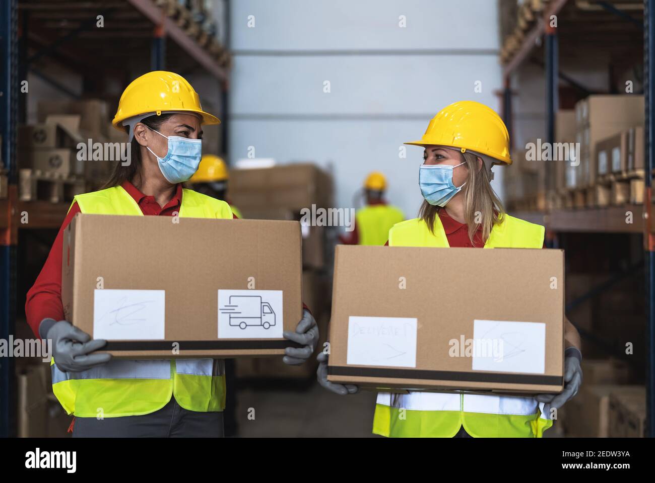 Team working in warehouse loading delivery boxes while wearing face surgical mask during corona virus pandemic - Logistic and industry concept Stock Photo