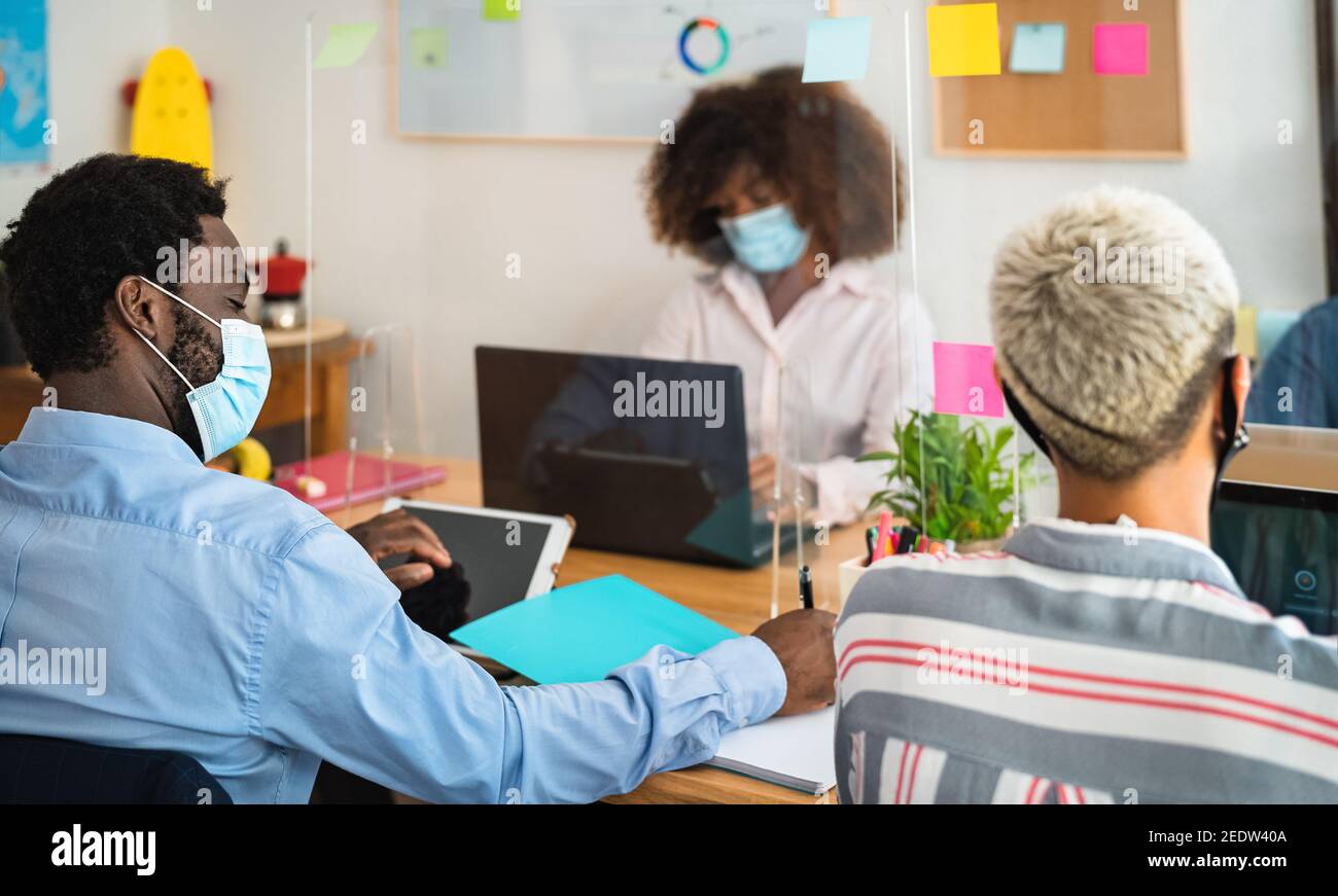 Young people in co-working creative space wearing surgical mask and keeping social distance to avoid corona virus spread Stock Photo