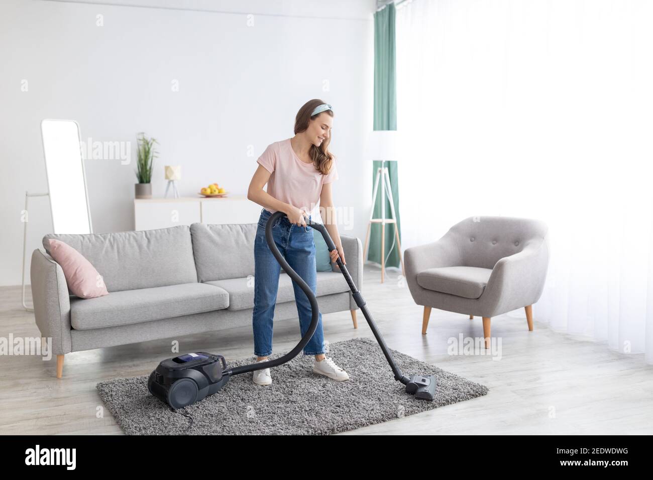 Cheerful female housekeeper using vacuum cleaner to tidy apartment