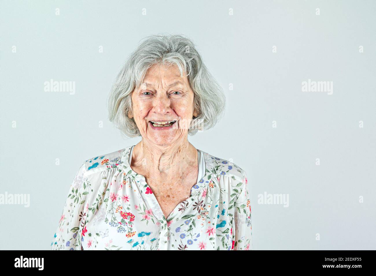 Elderly woman in her 80's with Gray hair isolated on a white backdrop smiling and laughing and happy. Stock Photo