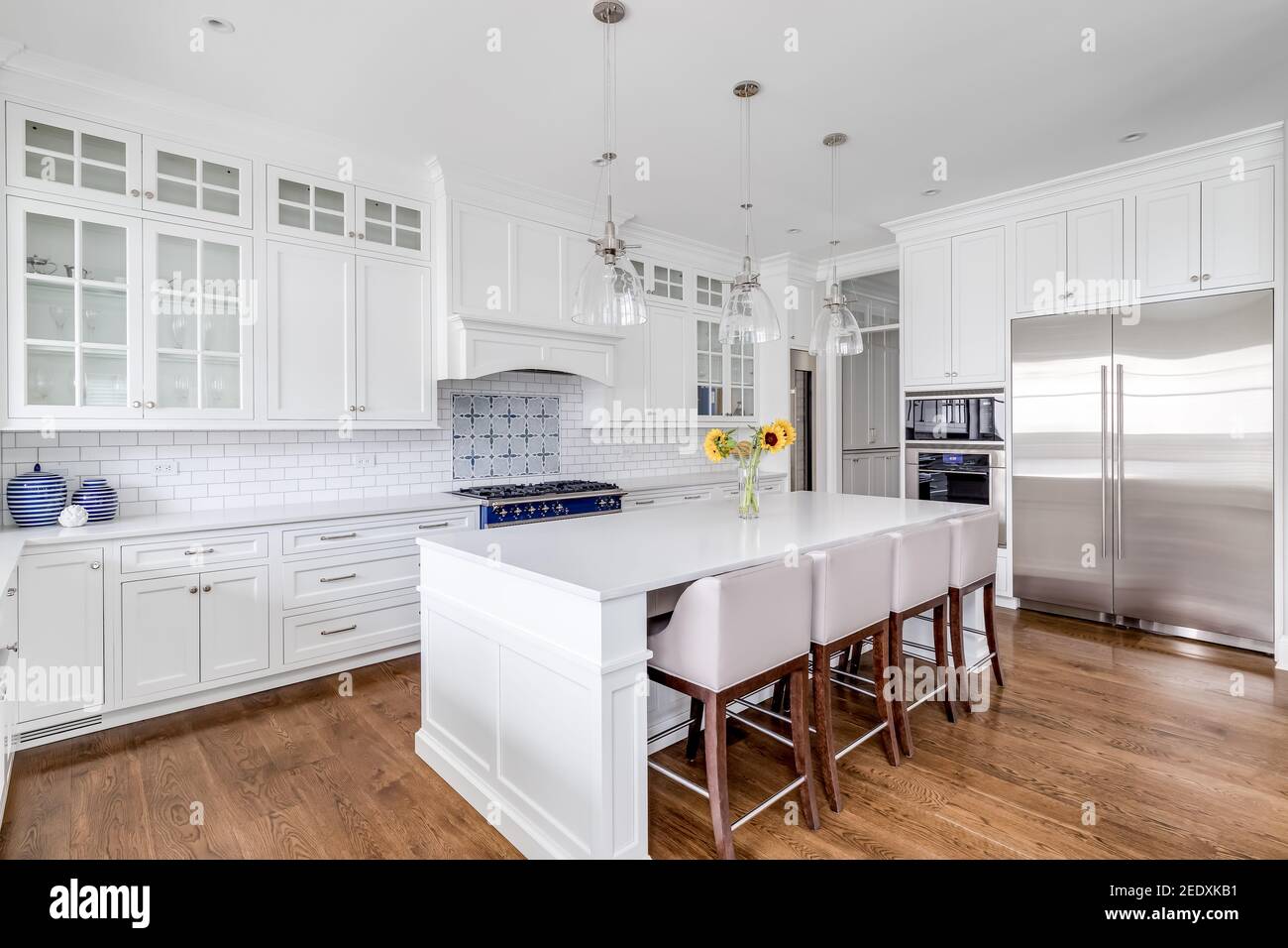 A luxury white kitchen with bar stools sitting at a large island, glass