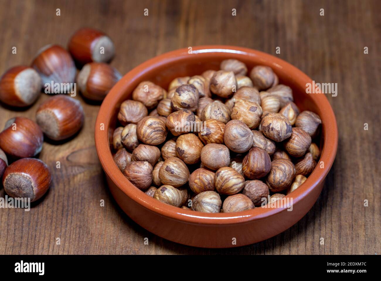 Peeled hazelnuts in bowl and hazelnuts in shell on rustic wooden table Stock Photo