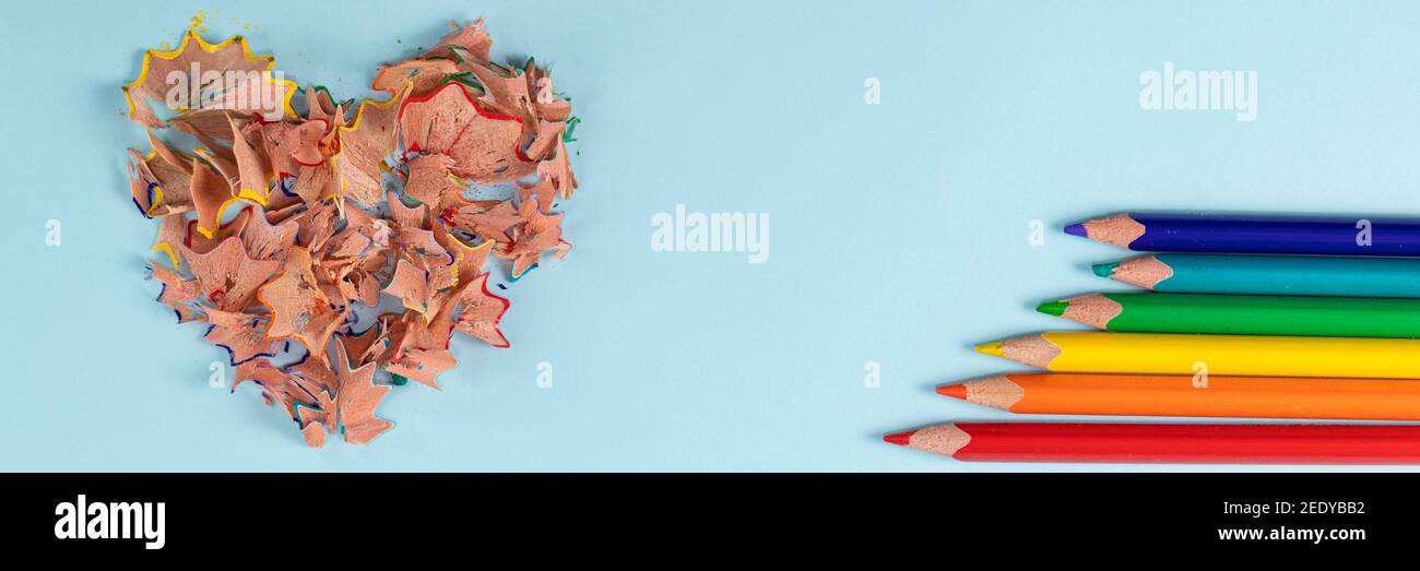 Banner with sharpened colored pencils and heart-shaped pencil shavings on pastel blue color. Rainbow or LGBT pencils. Decoration for St. Valentine's Day. Top view Stock Photo