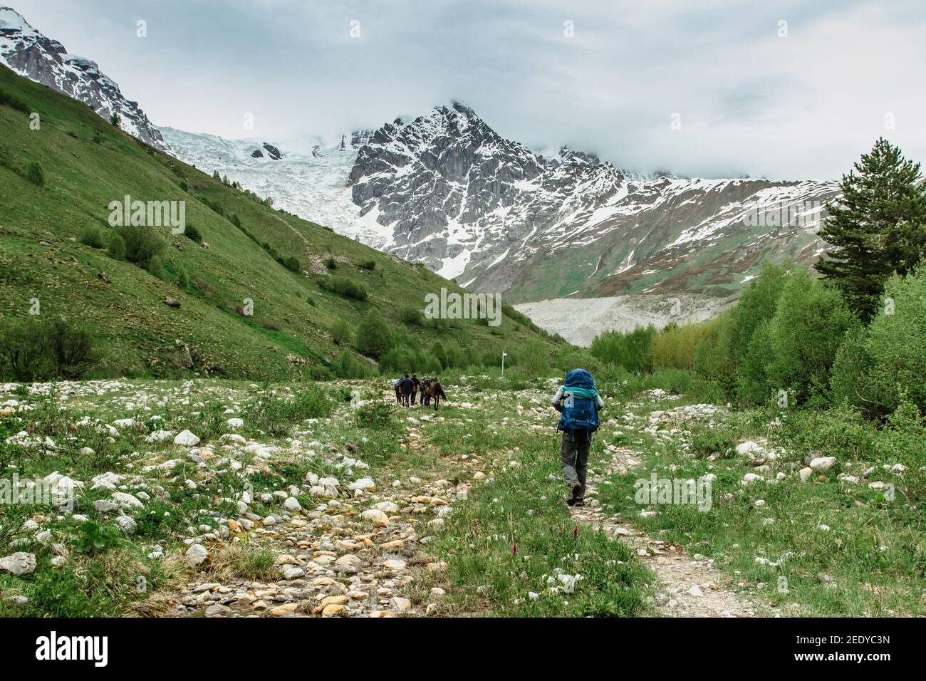 Active male traveller lost in snowy mountains,Georgia.Backpacker exploring Greater Caucasus.Wild pure nature,iceberg,horse on pasture.Popular travel Stock Photo
