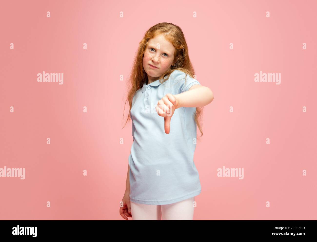 Thumb down, dislike. Happy, smiley redhair girl isolated on pink studio background with copyspace for ad. Looks happy, cheerful. Childhood, education, human emotions, facial expression concept. Stock Photo