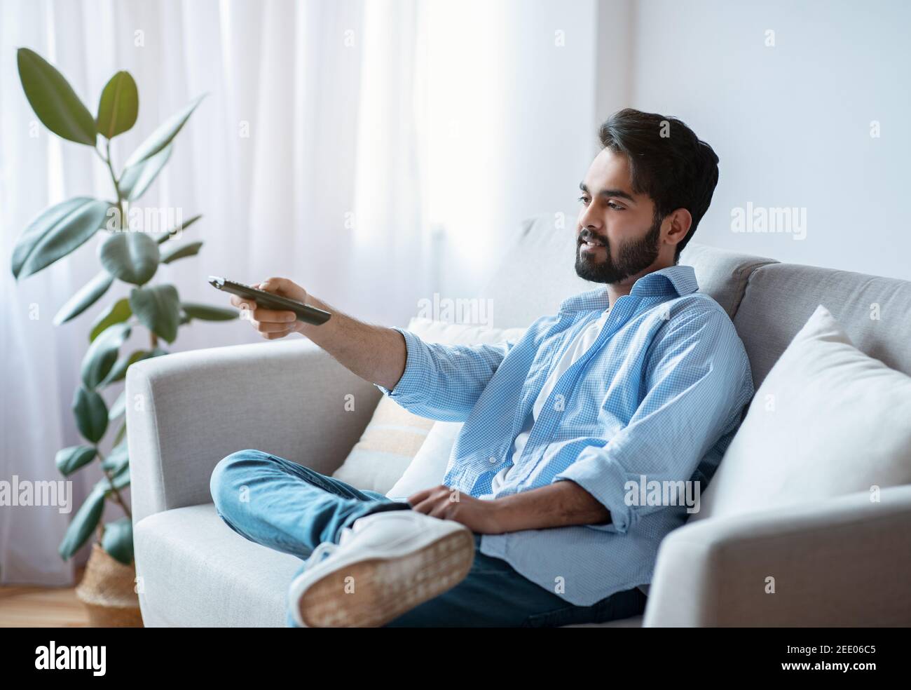 Arab man with remote controller switching channels while watching tv at home Stock Photo
