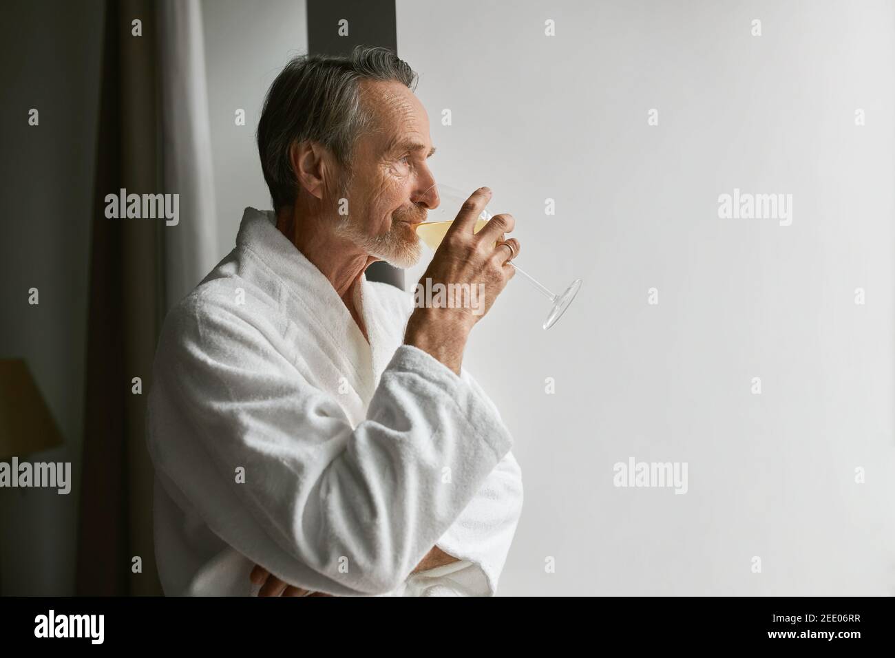 Side view of an elderly man drinking wine while looking at window Stock Photo