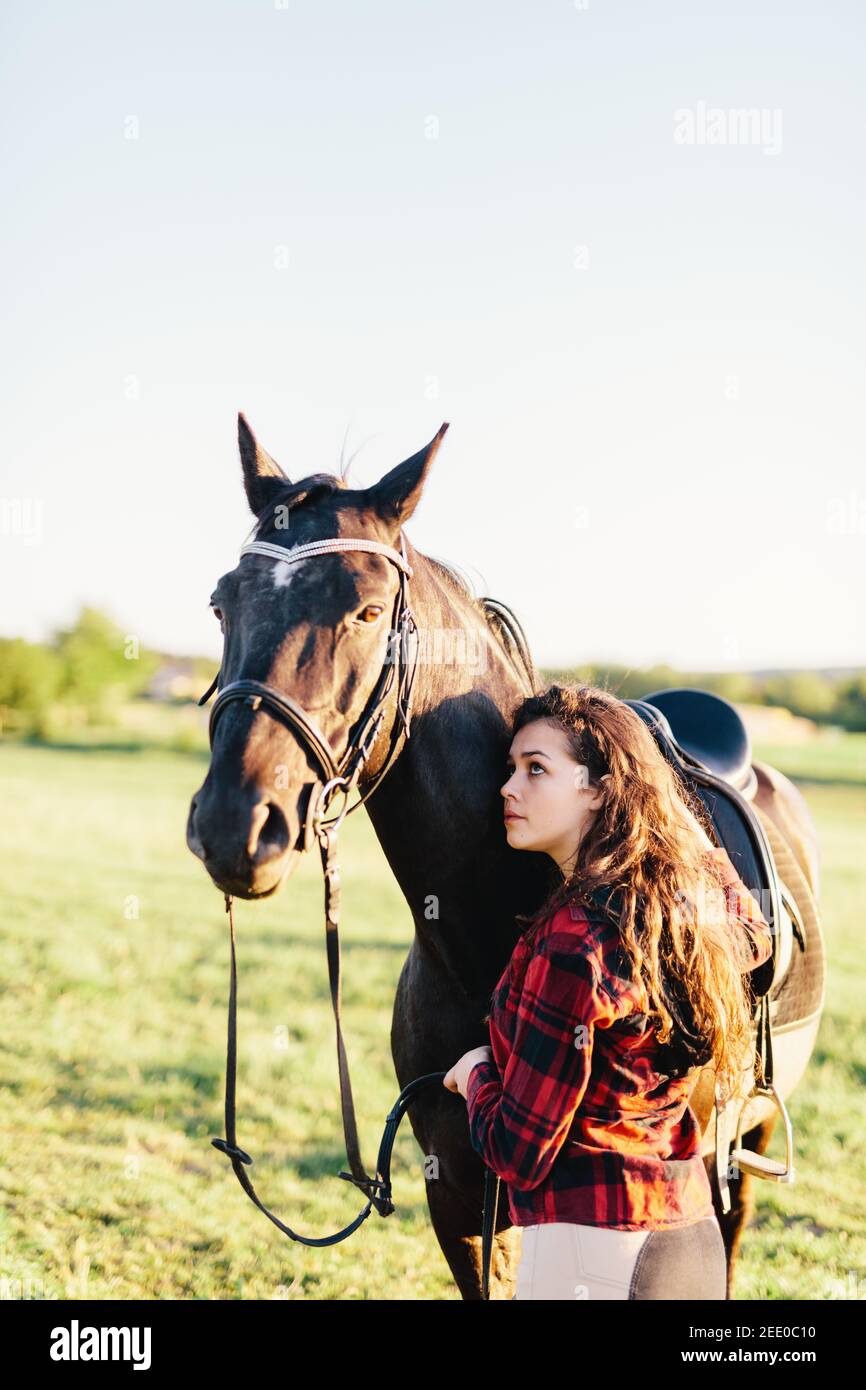 Young girl hugging purebred black horse on the field. Human and animal