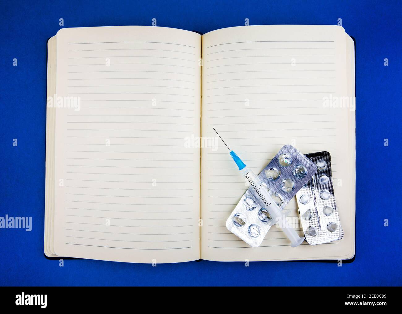 Blank Writing Pad and Empty Pack of the Pills and a Syringe on the Blue Paper Background closeup Stock Photo
