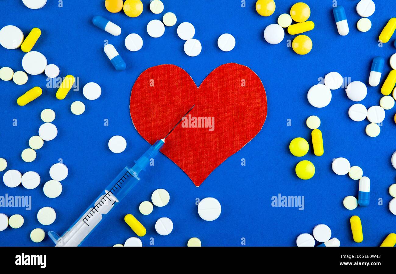 Heart Shape with a Pills and a Syringe on the Blue Paper Background Stock Photo