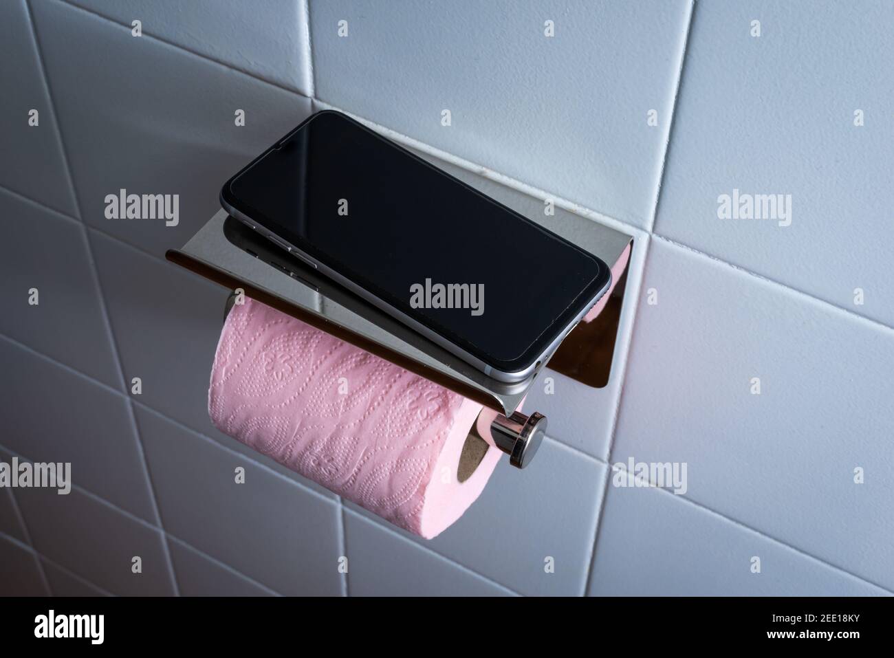 Mobile phone in toilet with pink toilet paper against white tile