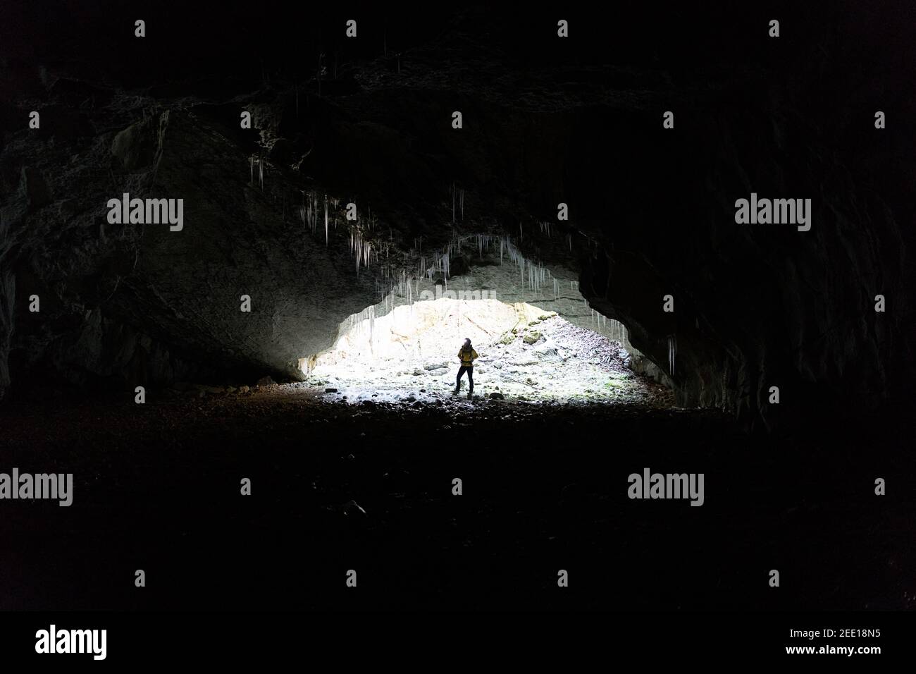 Woman standing at the entrance of a cave, illuminated by a backlight, stalagmites made of ice on the top, Slovenia Stock Photo