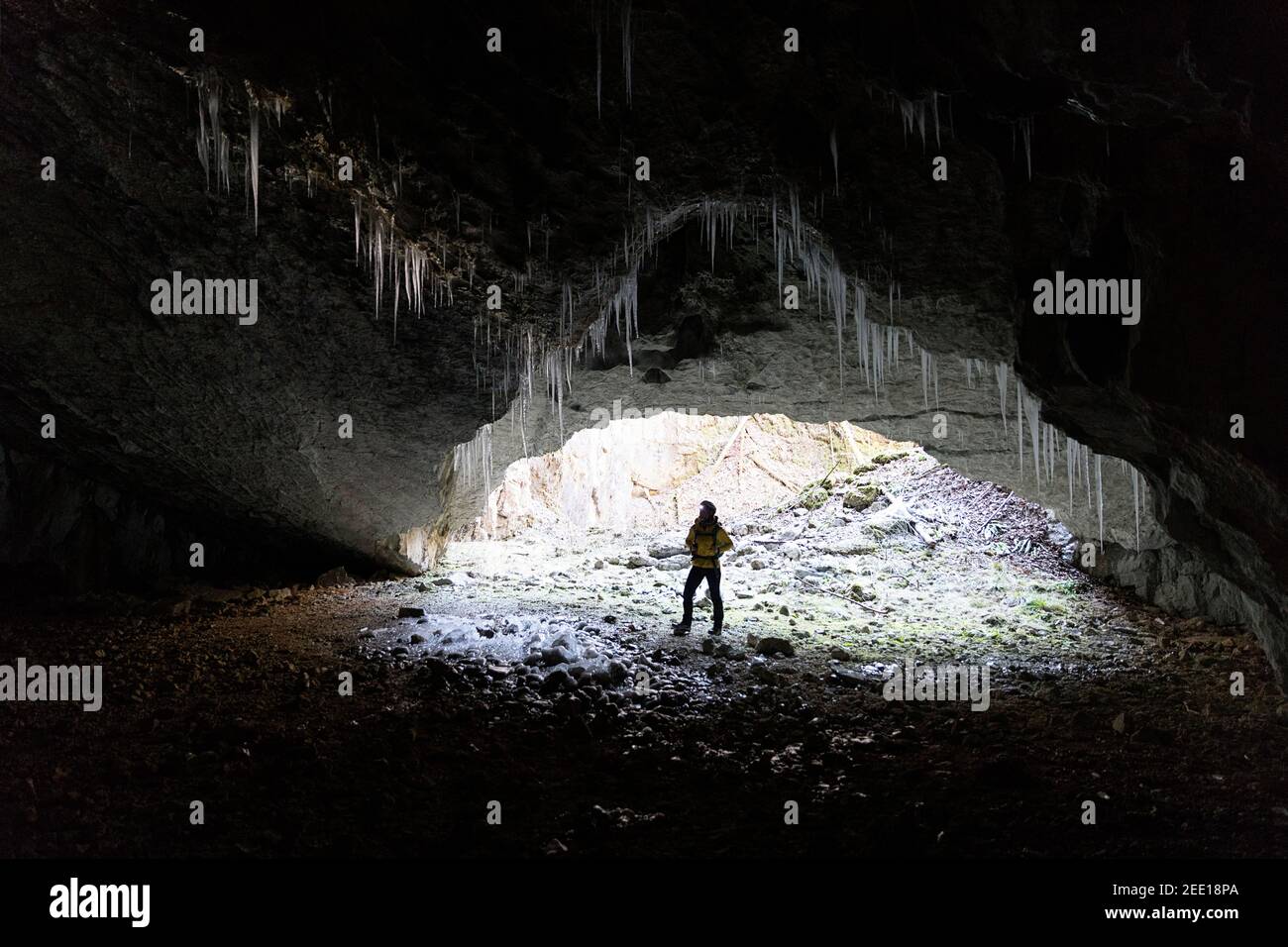 Woman standing at the entrance of a cave, illuminated by a backlight, stalagmites made of ice on the top, Slovenia Stock Photo