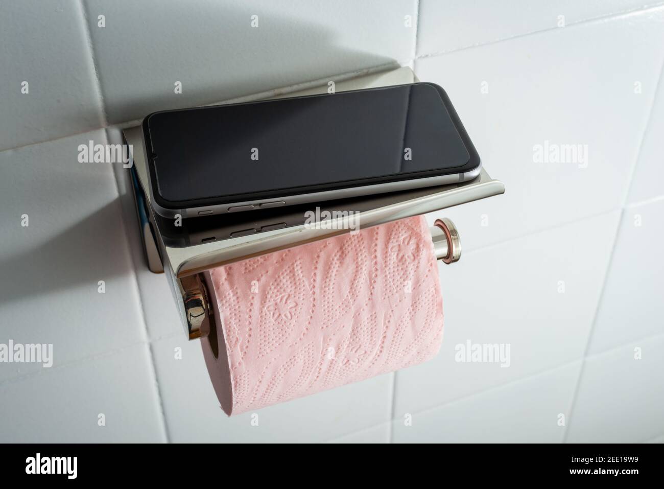 Mobile phone in toilet with pink toilet paper against white tile