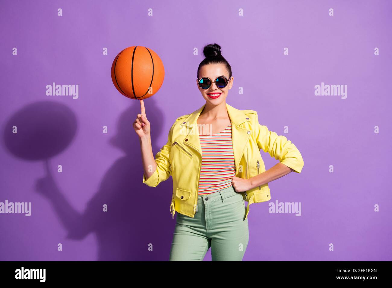 Photo of young happy positive smiling girl woman hold ball on finger wear green pants trousers isolated on violet color background Stock Photo