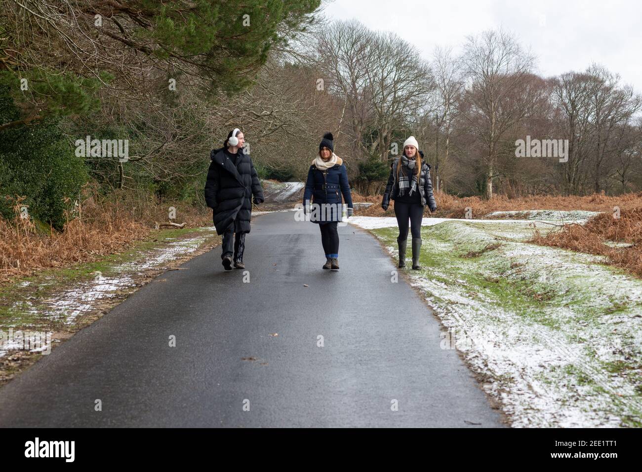 Three people walking down a country road with woolly hats and ear muffs in winter with snow Stock Photo