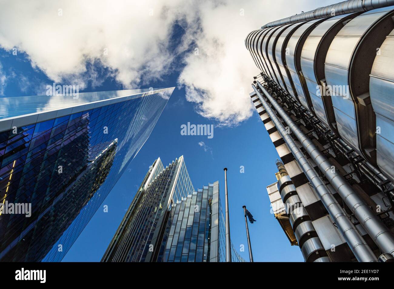 Dramatic upwards view of tall commercial buildings reaching up into a blue sky with fluffy white couds - Stock Image