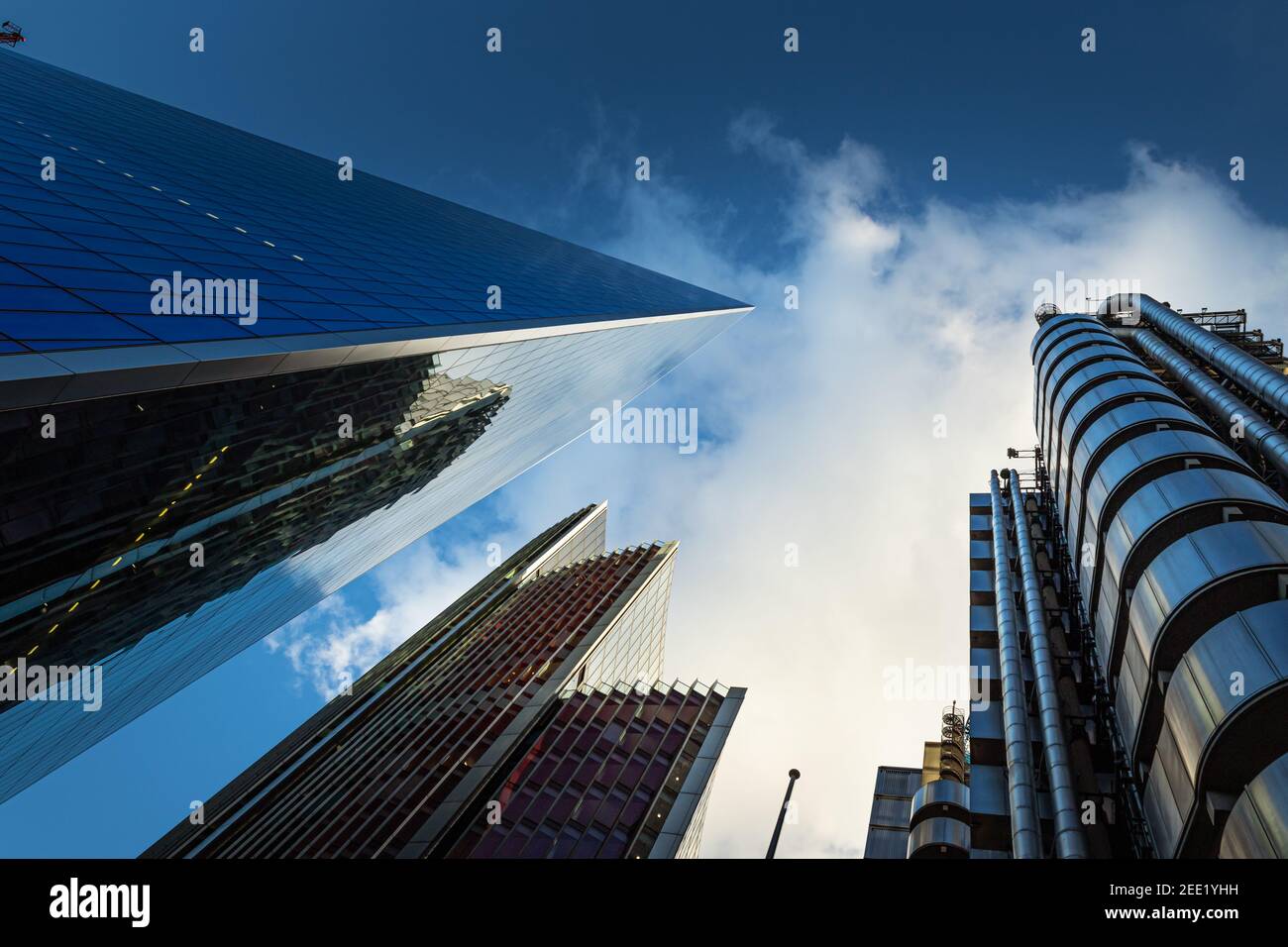 Dramatic upwards view of tall commercial buildings reaching up into a blue sky with fluffy white couds - Stock Image