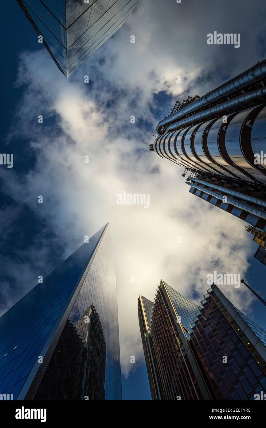 Looking up at tall commercial buildings reaching up into a dramatic deep blue sky with gaseous white couds - Stock Image
