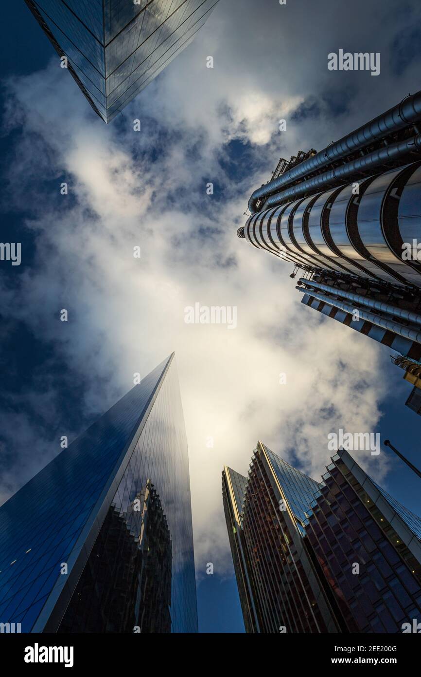Looking up at tall commercial buildings reaching up into a dramatic deep blue sky with gaseous white couds - Stock Image
