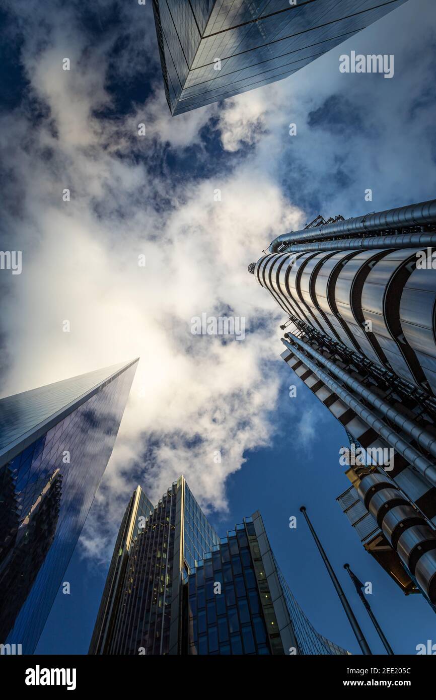 Looking up at tall commercial buildings reaching up into a dramatic deep blue sky with gaseous white couds - Stock Image