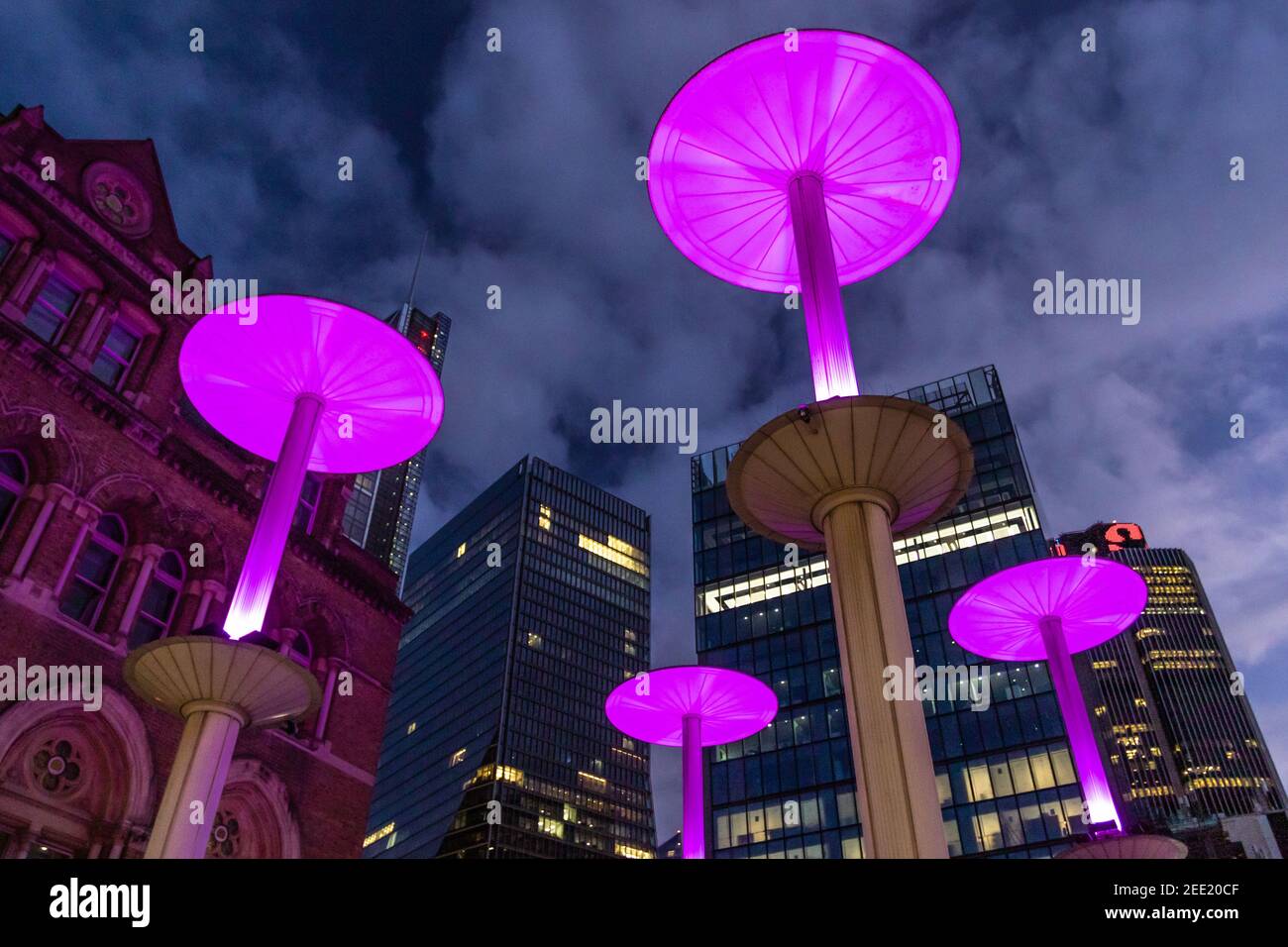 Illuminated pink mushroom lights at the entrance to Liverpool St Station against the background of the city at twilight - Stock Image
