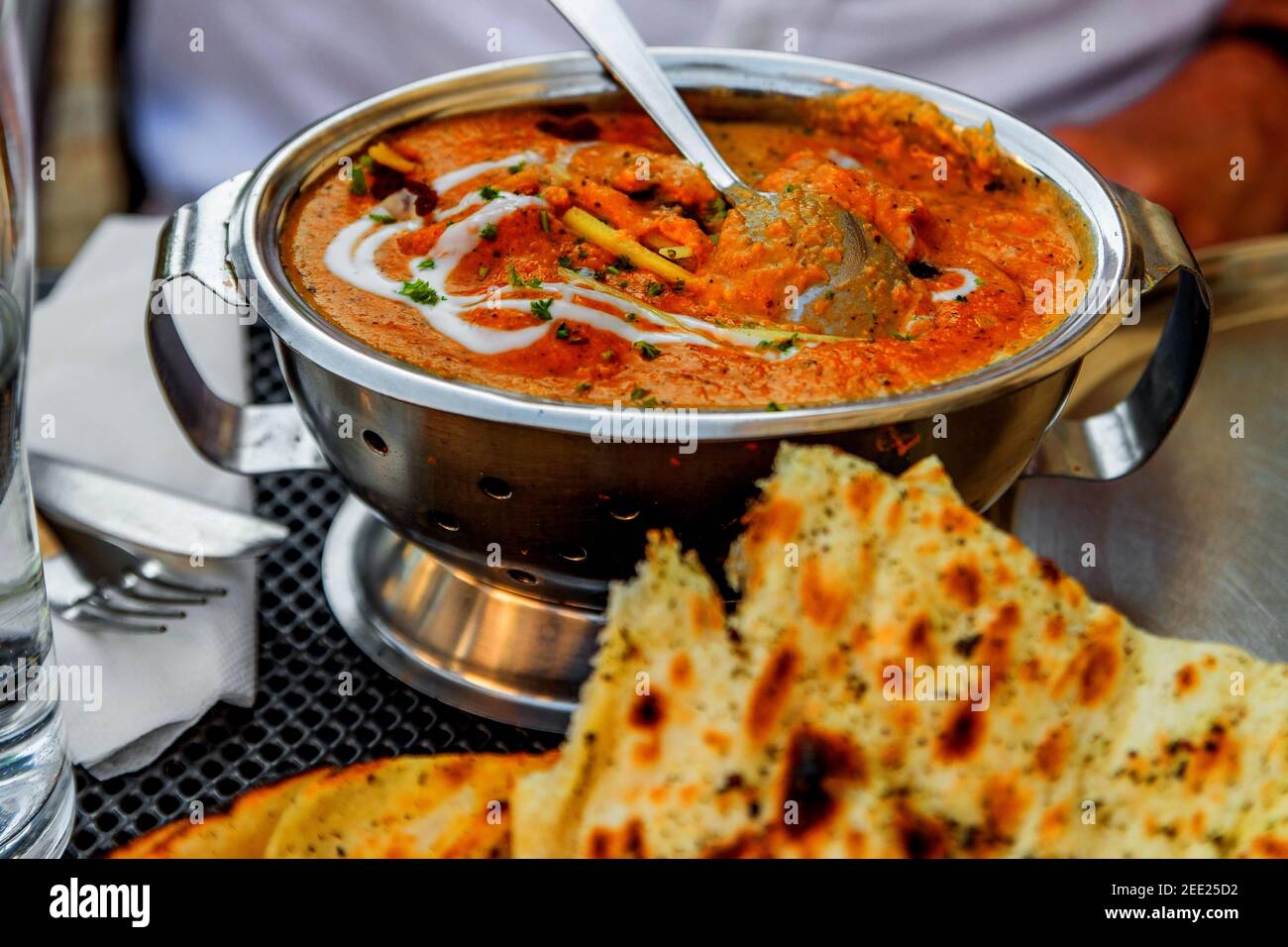 Bowl with indian meal chicken tikka masala, bread (butter naan), part of person at the table. Stock Photo