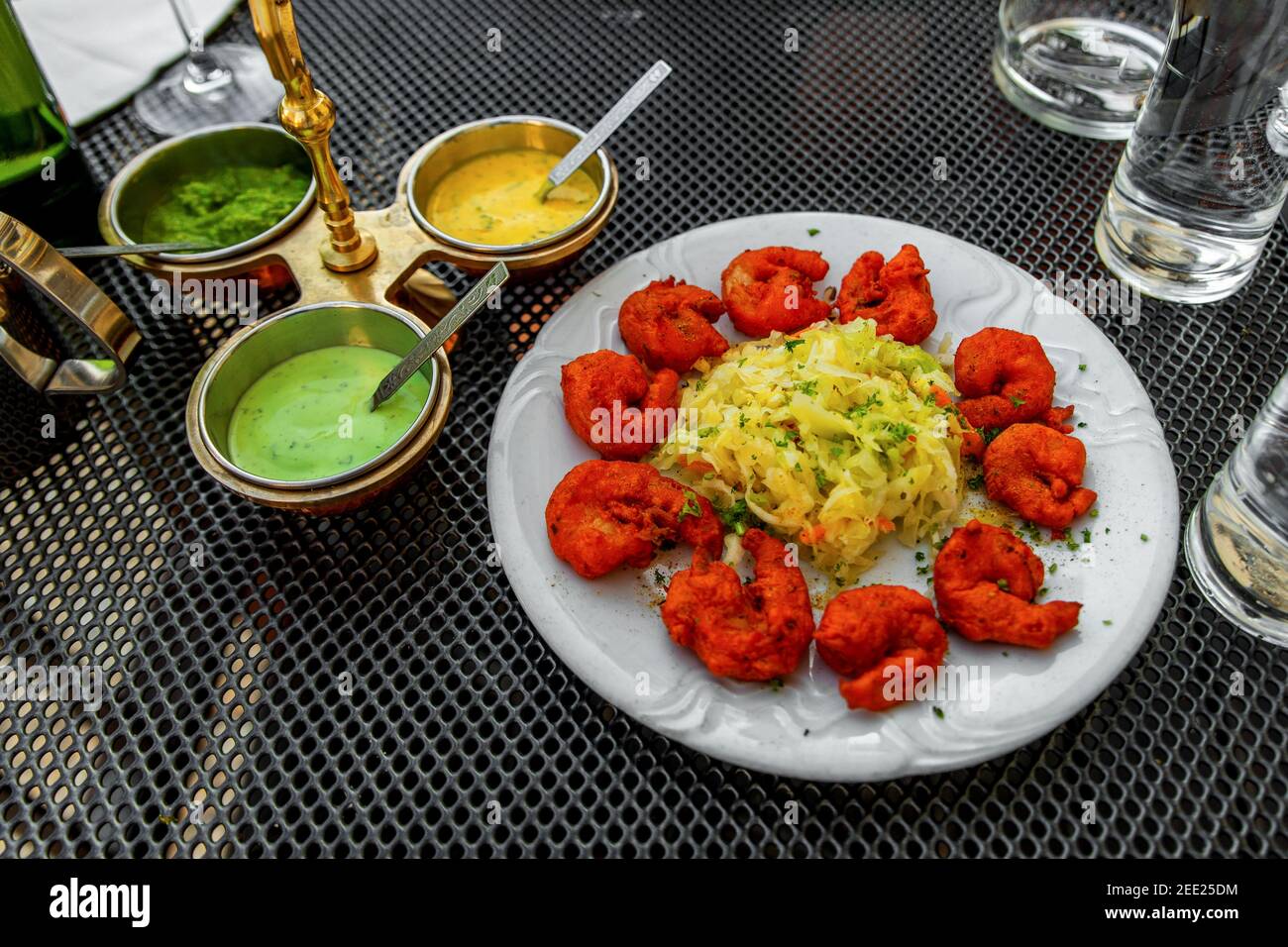 Fried breaded spicy shrimps with salad, three sorts of sauce (mint,curry,chili) in decorative bowl, glass of water on indian restaurant table outdoor Stock Photo