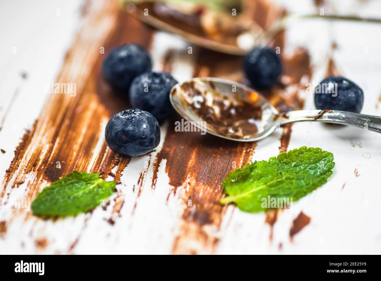 Blueberry, mint leaf and spoon dirty from chocolate on dirty background with chocolate lines. Modern style food background. Stock Photo