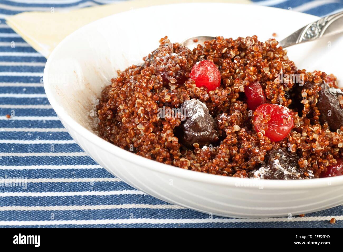 Dessert from boiled quinoa seeds with pdried plums and cherries sprinkled with sugar in plate on blues tripes table cloth. Stock Photo
