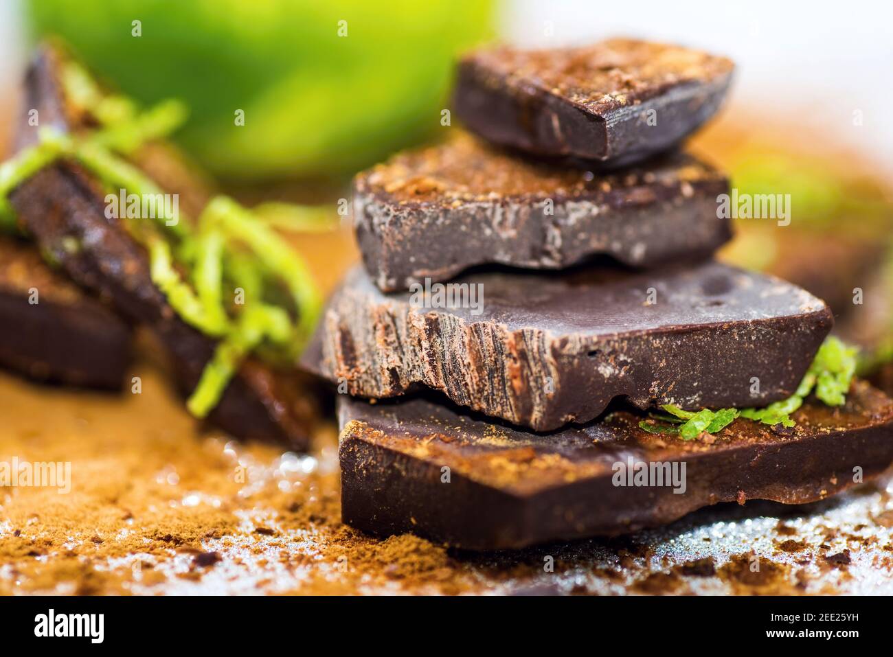 Broken pieces of chocolate sprinkled with cinnamon and lime peel, lime fruit on background. Stock Photo