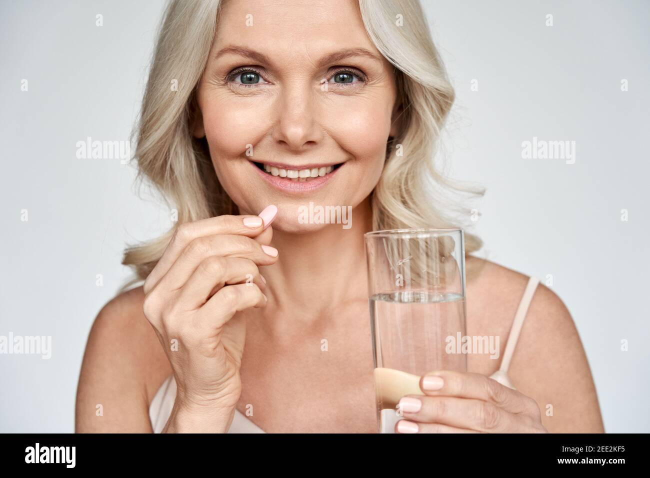 Smiling healthy middle aged 50s woman taking supplement vitamin pill. Stock Photo