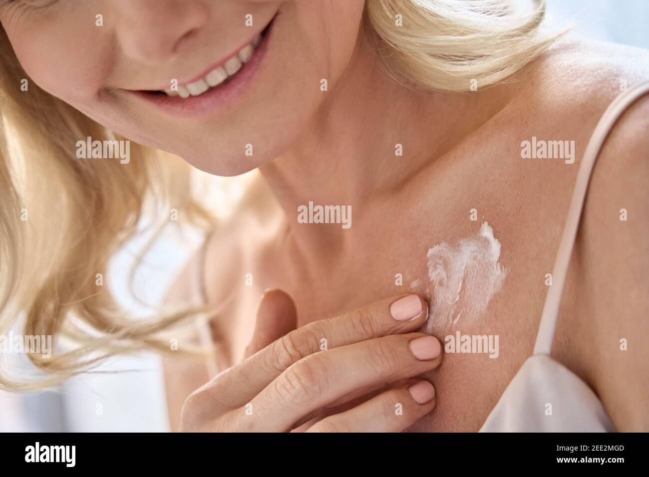Happy middle aged woman applying cream moisturizing lotion on body skin. Stock Photo