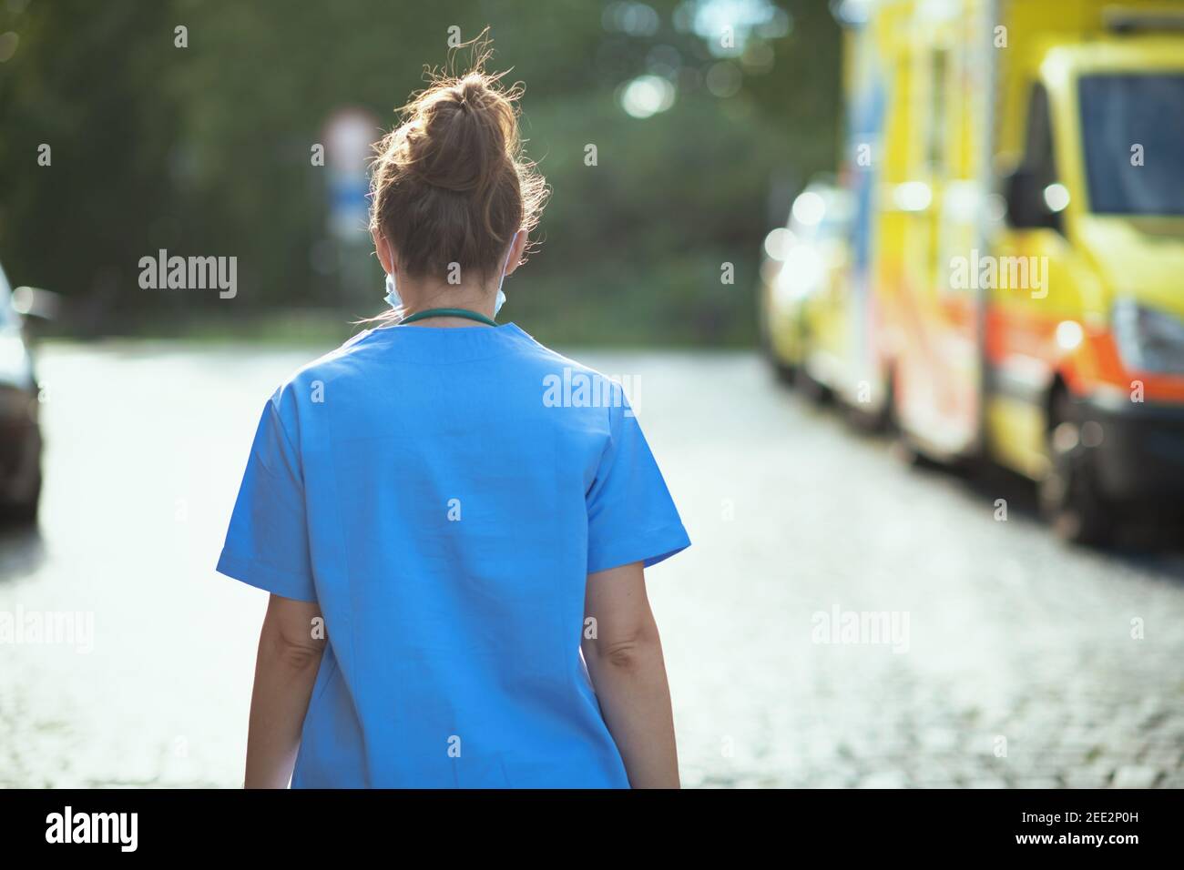 covid-19 pandemic. Seen from behind medical doctor woman in scrubs outside near ambulance walking. Stock Photo