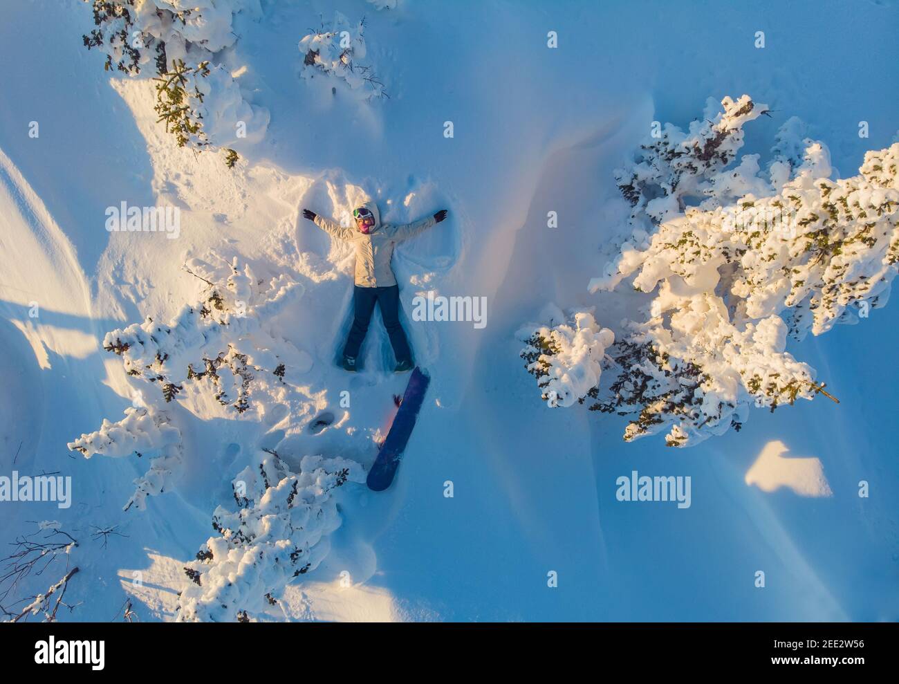 Snow angel, girl snowboarder lies with snowboard in winter forest, aerial top view. Stock Photo